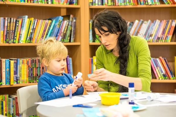 A woman helping a child with crafts in a library