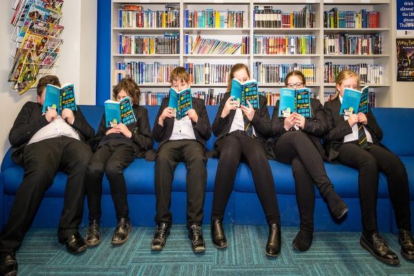 6 children in school uniforms sat on a sofa with books up to their faces