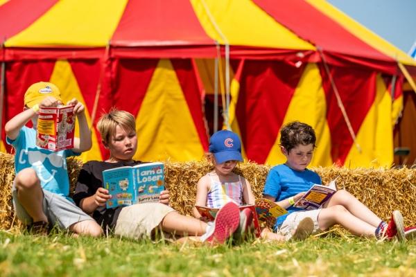 4 children reading sat outside a red and yellow tent